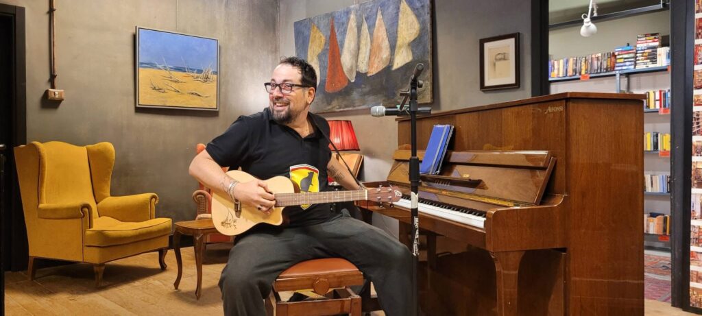 Napodano dal vivo, seduto con ukulele davanti al pianoforte e rivolto verso il pubblico